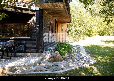 Rustica casa in legno circondata da alberi e piante, con un sentiero in pietra che conduce all'ingresso, sotto la luce del giorno. Foto Stock