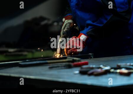 Lavoratore che smeriglia con cura un pezzo di metallo, scintille che volano dalla smerigliatrice angolare in officina. Foto Stock