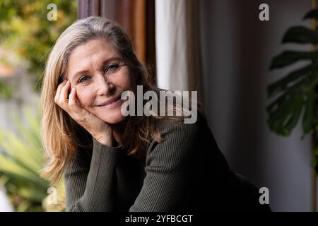Donna anziana sorridente che gode di un momento tranquillo dalla finestra a casa Foto Stock