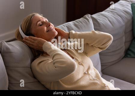 Rilassati sul divano, donna anziana che ascolta musica con le cuffie a casa Foto Stock