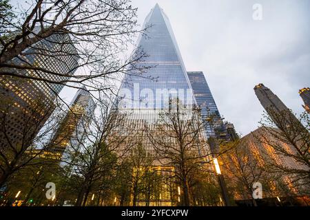 Una suggestiva vista dall'angolo basso dell'One World Trade Center di New York, incorniciata da alberi e grattacieli circostanti. Foto Stock