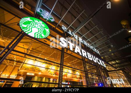 Una vista notturna di una caffetteria Starbucks a New York City, caratterizzata da un logo illuminato e da una facciata in vetro che riflette le luci della città. Foto Stock