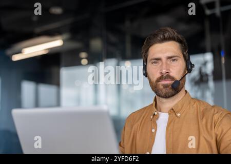 Uomo d'affari maturo che indossa una cuffia per videoconferenze mentre lavora in un ufficio moderno. L'espressione sicura riflette il comportamento professionale. L'interazione enfatizza l'impostazione del lavoro remoto. Foto Stock