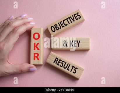 Obiettivi OKR e simbolo dei risultati chiave. Blocchi di legno con parole obiettivi OKR e risultati chiave. Mano d'affari. Bellissimo sfondo rosa. Affari Foto Stock