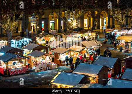 Vista dall'alto sulla piazza serale della città con chioschi in legno illuminati e gente sul tradizionale mercato di Natale di Asti, Italia. Foto Stock