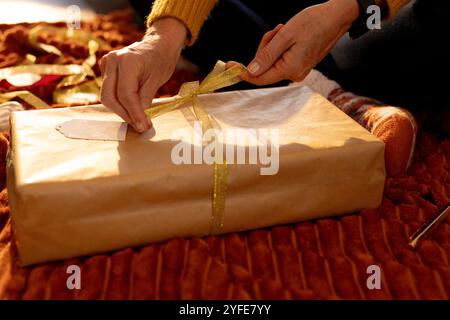 Avvolgere il regalo di Natale con il nastro dorato, le mani legano l'arco in regalo, a casa Foto Stock