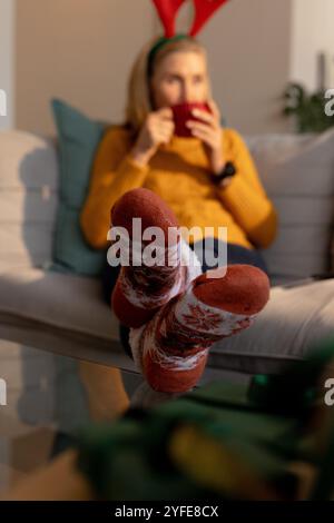 Periodo natalizio, relax a casa, donna anziana in calze festive gustando una bevanda calda Foto Stock