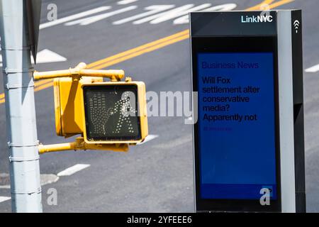 Un segnale di attraversamento pedonale con una figura bianca si trova accanto a un chiosco digitale LinkNYC che mostra notizie di affari in una strada della città di New York City Foto Stock