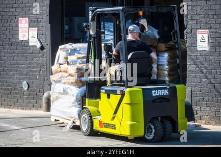Lavoratore che utilizza un carrello Clark che sposta un pallet di merci in una banchina di carico. Foto Stock
