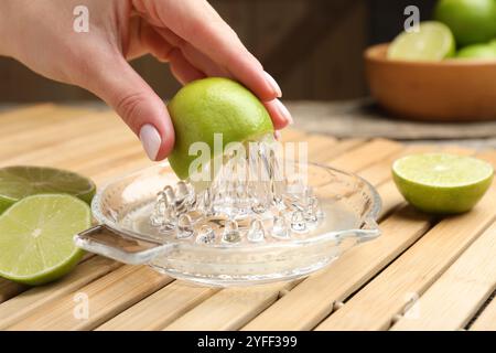 Donna che spreme il succo di lime fresco con la centrifuga al tavolo di legno, primo piano Foto Stock