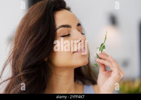 Una giovane donna con lunghi capelli scuri tiene un rametto di microgreen fino al naso, godendo dell'aroma fresco Foto Stock