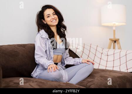 Vesti la donna atletica in un abbigliamento sportivo seduto su un comodo divano a casa, godendoti un momento di relax dopo l'allenamento Foto Stock