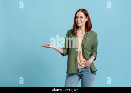 Una giovane donna con i capelli rossi gesta con la mano per presentare un prodotto o un servizio, con un atteggiamento allegro e sicuro Foto Stock