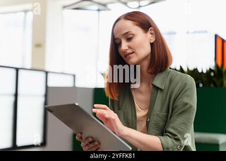 Una donna d'affari utilizza un tablet digitale e naviga su Internet in un moderno ufficio con grandi finestre Foto Stock