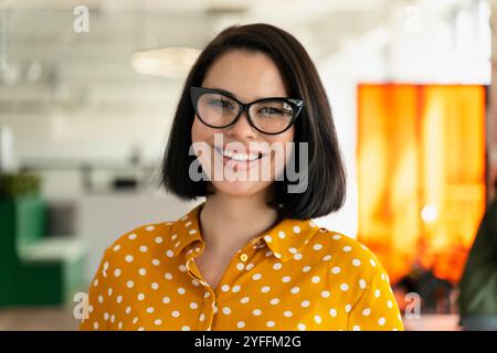 Giovane donna d'affari sicura di sé in un ufficio moderno, sorridente. Trasuda positività e professionalità, mostrando il suo atteggiamento amichevole Foto Stock