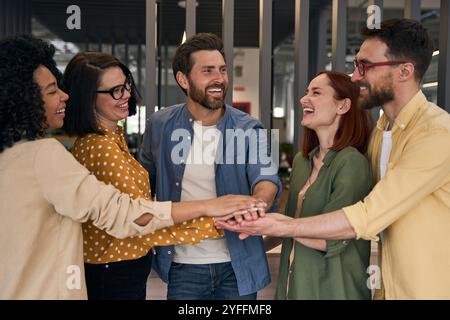 Diversi team di colleghi stanno mettendo le mani insieme, ridendo e festeggiando un successo in ufficio Foto Stock