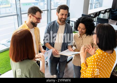 In un ufficio moderno si riuniscono diversi team di professionisti, impegnati in una vivace discussione su un rapporto finanziario Foto Stock