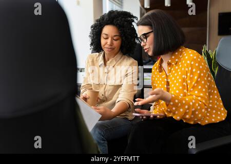 Due donne d'affari stanno avendo una riunione informale in un ufficio moderno, discutendo documenti e idee Foto Stock