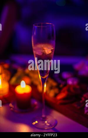 Bicchiere di champagne sul tavolo con luce viola al neon, concetto di festività ed eventi festivi Foto Stock