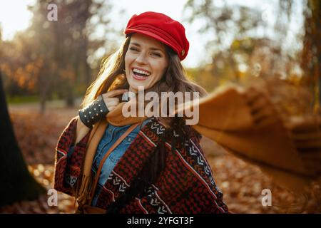 Ciao autunno. giovane donna sorridente in cappello rosso con sciarpa nel parco cittadino. Foto Stock