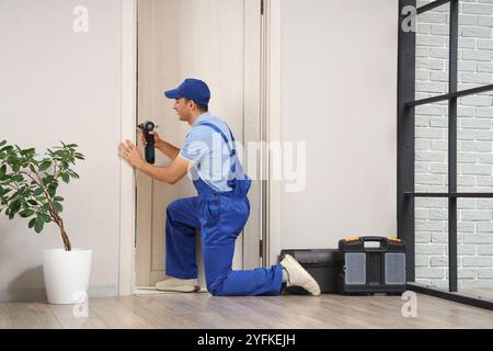 Lavoratore maschio con trapano elettrico che installa la piastra di battuta della porta a casa Foto Stock