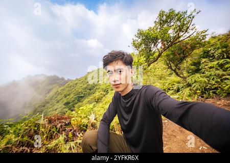 Uomo in piedi orgoglioso sulla vetta della montagna, rivolto verso la fotocamera. Splendida vista dalla cima. Foto Stock