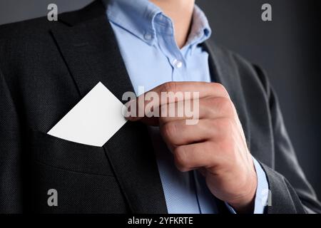 Uomo che prende un biglietto da visita vuoto dalla tasca della giacca su sfondo grigio, primo piano. Mockup per il design Foto Stock