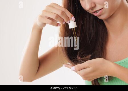 Una giovane donna applica una goccia di olio da una pipetta ai capelli, primo piano. Vitamine, cheratina per il trattamento, il rafforzamento e la crescita dei capelli. Problemi Foto Stock