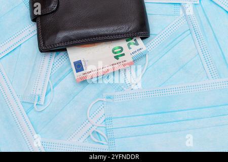 Nero uomo portafoglio con euro soldi dentro sul blu monouso maschere mediche viso. Permuta maschere mediche. Affari durante una pandemia o un'epidemia Foto Stock