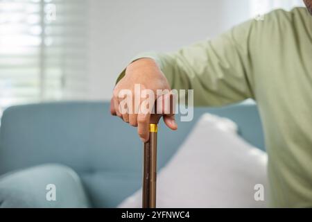 Asian Old Man con occhiali che battono per alzarsi dal divano con bastone da passeggio Foto Stock