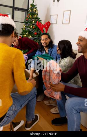 Scambiare regali con l'albero di natale, amici multirazziali sorridenti gioiosamente, a casa Foto Stock