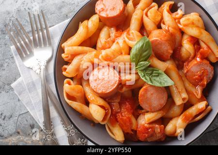 Treccione a spirale con salsicce affumicate in salsa piccante di pomodoro da vicino nel recipiente sul tavolo. Vista dall'alto orizzontale Foto Stock