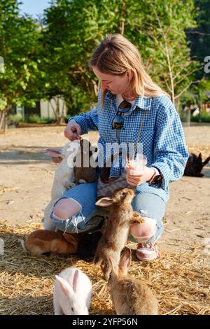 Una giovane donna ama divertirsi con un gruppo di conigli in una tranquilla fattoria durante un pomeriggio di sole Foto Stock