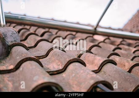 Primo piano di tegole rustiche in argilla con un motivo ondulato, con una struttura tubolare in metallo sopra. La texture resistente agli agenti atmosferici e le macchie muschiate aggiungono carattere alla ro Foto Stock