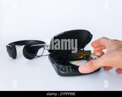Primo piano della mano di un uomo che inserisce un compact disc in un lettore di compact disc con cuffie isolate su sfondo bianco. Foto Stock