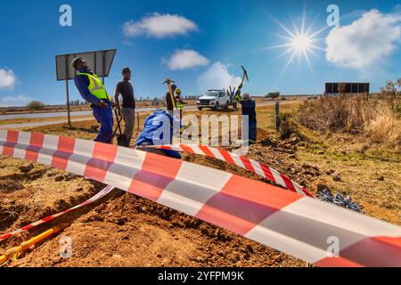 squadra di operai di costruzione africani in un fosso di trincea che ripara tubi di fissaggio con piccone e pale, nastro da barricata, scavando una trincea laterale Foto Stock