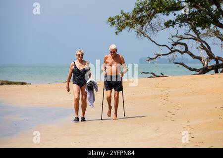 Coppie anziane che camminano sulla sabbia sullo sfondo del mare. Donna e uomo con bastoni su una spiaggia tropicale, vita in pensione Foto Stock