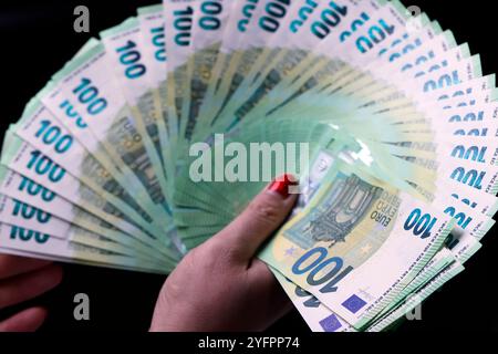 La mano femminile tiene in mano moneta europea Euro su sfondo nero: Banconote in euro da 100 euro. Tema dell'inflazione, delle imprese, dell'economia e della finanza. Foto Stock