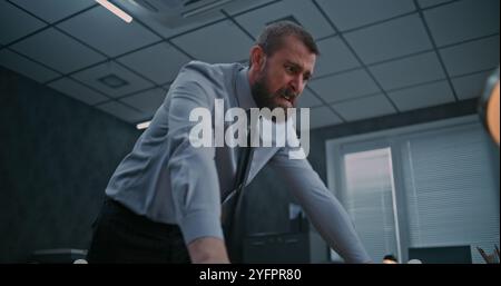 Un uomo d'affari aggressivo perde il suo temperamento in un attacco di rabbia. Un dipendente dell'ufficio furioso rompe il monitor del computer con la tastiera, getta le cose dal desktop e urla. Crisi finanziaria o licenziamento. Foto Stock