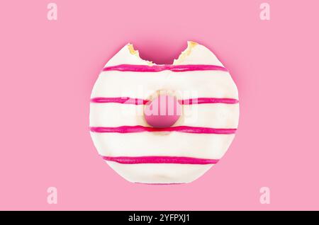 Manca un boccone di ciambella al cioccolato bianco e a righe rosa su sfondo rosa. Foto Stock