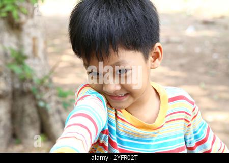 Un ragazzo allegro con un grande sorriso ama giocare all'aperto con una colorata camicia a righe. La sua espressione gioiosa cattura l'essenza della felicità dell'infanzia Foto Stock