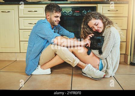 Coppia felice, animale domestico e gioco con il cane sul pavimento della cucina per la cura, mattina e amore per il cucciolo carino. Uomo, donna e rilassati con il cucciolo per giocare Foto Stock