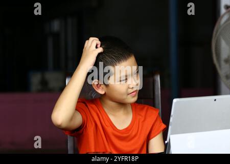 Un ragazzo si vede graffiare la testa nel pensiero mentre usa un tablet. Questa immagine cattura l'essenza dell'apprendimento e della curiosità in un educato moderno Foto Stock