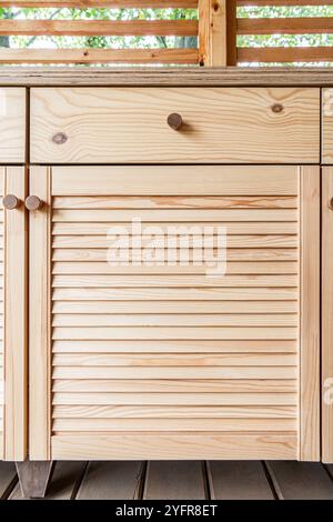 Armadi in legno di cucina esterna con porte a sfinestratura, cassetti, maniglie in legno e un ripiano in compensato bianco si stagliano su una terrazza in legno vista ravvicinata Foto Stock