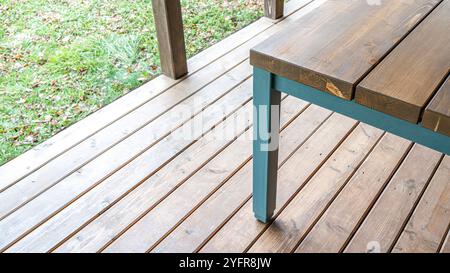 Il tavolo da pranzo e' fatto di legno di pino con gambe blu sulla terrazza con pavimento in legno e ha una vista della vicina area erbosa Foto Stock