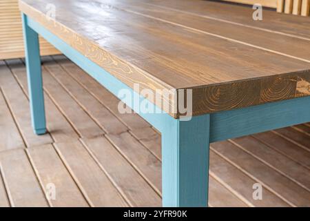 Il tavolo da pranzo e' realizzato in legno di pino con le gambe blu vista ravvicinata. Enorme tavolo sulla terrazza con pavimento in legno e vista della vicina area erbosa Foto Stock