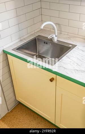 Cucina con armadi gialli con manici in legno e piano di appoggio in plastica con finitura in marmo. Piano di lavoro in plastica con superficie terminale verniciata verde Foto Stock