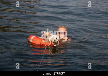 Una donna e il suo cane galleggiano serenamente in acque tranquille, supportate da un salvagente arancione Foto Stock