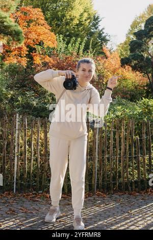 Bella giovane donna scatta foto con una fotocamera professionale nella foresta autunnale. Ragazza sorridente che si gode il tempo autunnale. Riposo, relax, stile di vita conc Foto Stock