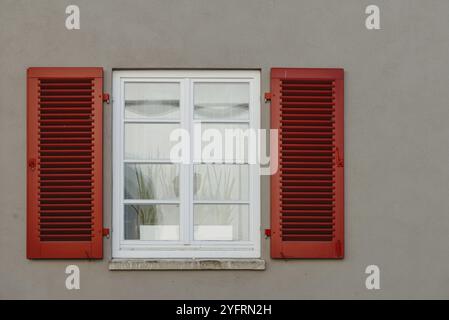 Finestre italiane sulla facciata bianca della parete con persiane classiche di colore rosso aperto e fiori sulle finestre Foto Stock